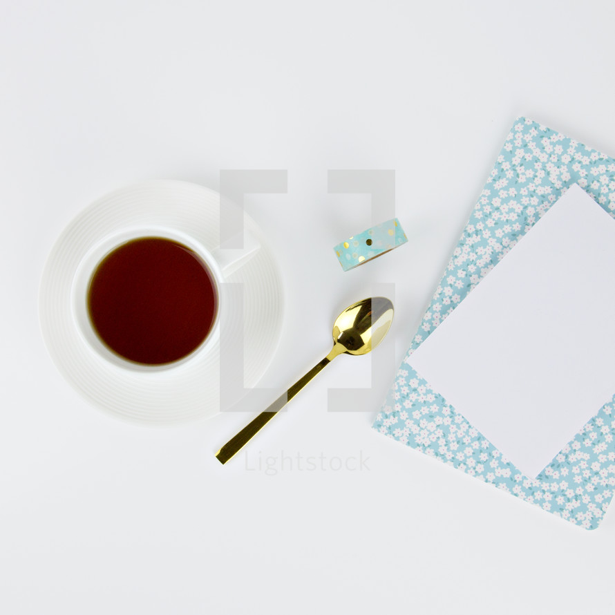 coffee cup, gold spoon, tape roll, planner, and white paper 