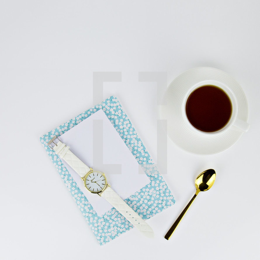 watch, floral planner, coffee cup, gold spoon, and paper on white background 