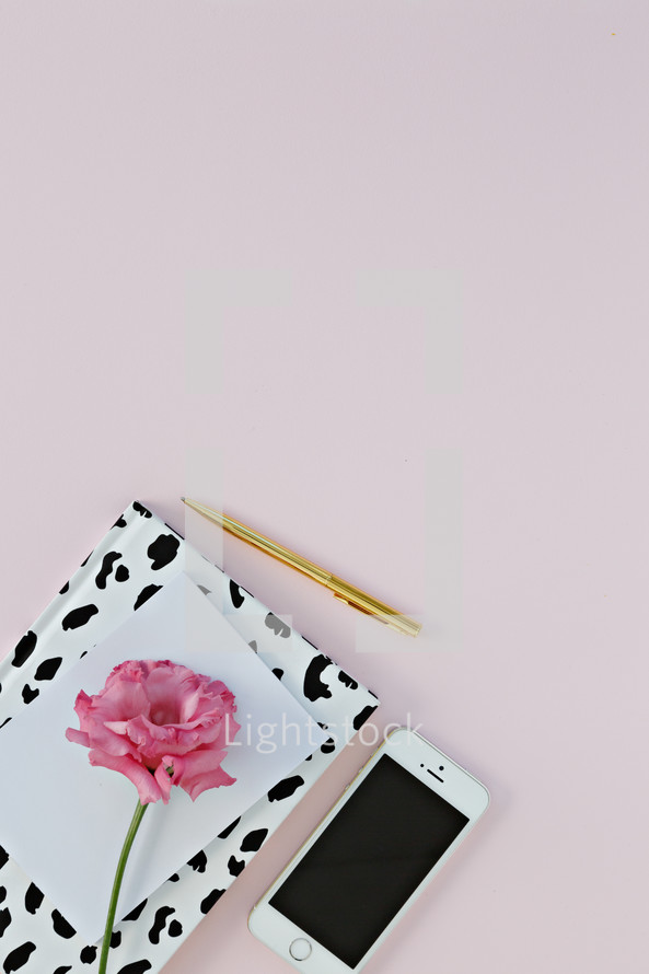 pink carnation, paper, notebook, pen, and cellphone on a pink background 