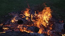 Closeup of flames and coals of camp fire burning wood logs and tree branches in cinematic slow motion.