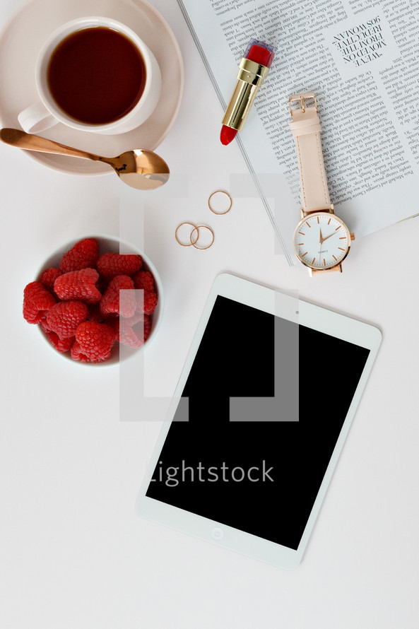 Raspberries in a bowl, watch, lipstick, tablet, magazine, rings, spoon, and coffee cup