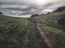 rutted path or road going through the hillside with a cloudy sky