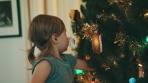 toddler girl hanging ornaments on a Christmas tree 