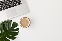 laptop computer, coffee cup, and tropical leaf on a white desk 