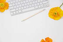 computer keyboard, pencil, and yellow and orange poppies on white 