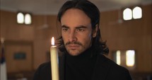 Serious, thoughtful, contemplative man in church holding a burning, lit candle stick.