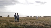 Two young men encounter Jesus, an angel or spiritual figure in white cloak standing in the distance in cinematic slow motion.