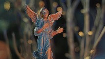 Close Up of an archangel with outstretched wings announcing the Nativity. Ceramic figure lit by the fire in the fireplace. Retro Christmas decoration. Dolly Shot and bokeh lights
