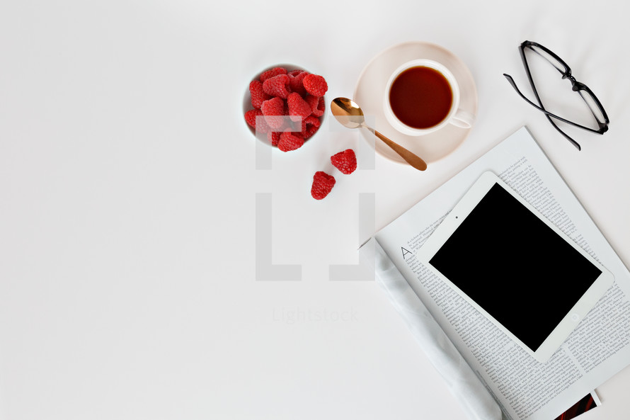 Raspberries in a bowl, reading glasses, magazine, spoon, and coffee cup