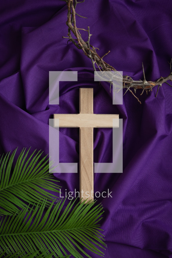 Cross, crown of thorns and palm leaves on a purple cloth background