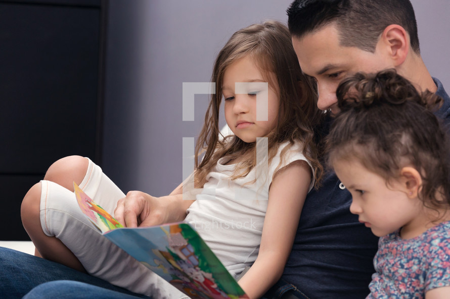 Man Reading a book to his two daughters 