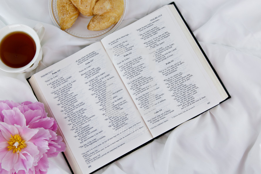 croissant, tea cup, pink flowers, and open Bible 