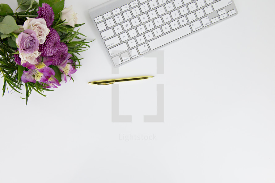 flower arrangement, pens, and computer keyboard on a white desk 