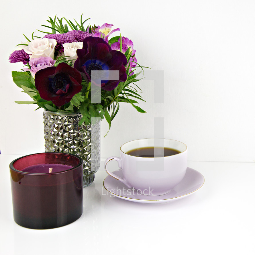 purple flower arrangement, candle, tea cup on a table 