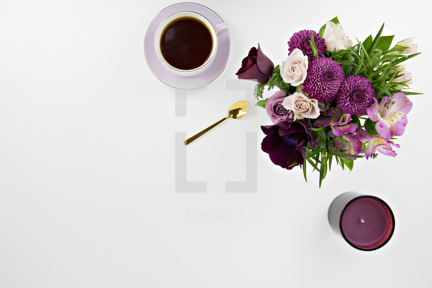 tea cup, purple flower arrangement and candle on white background
