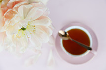tea cup, spoon, and flower petals on a pink background 