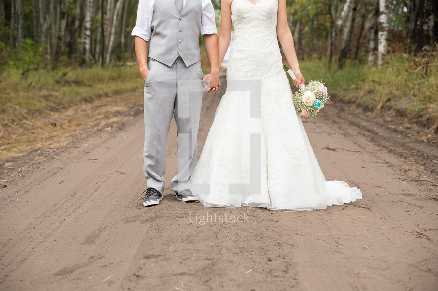 a bride and groom standing on a dirt road 