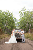 bride and groom standing on a dirt road in front of a vintage truck 