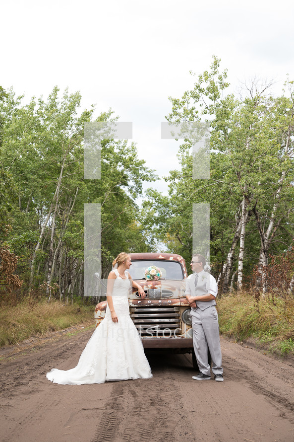 bride and groom standing on a dirt road in front of a vintage truck 