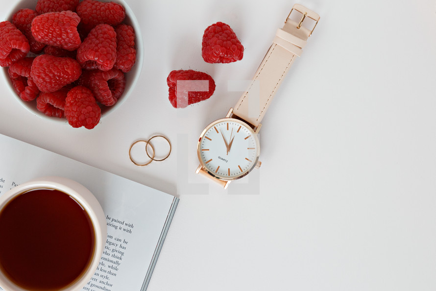 Raspberries in a bowl, watch, magazine, rings, and coffee cup
