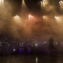 Man performing on stage and audience with lighters raised.
