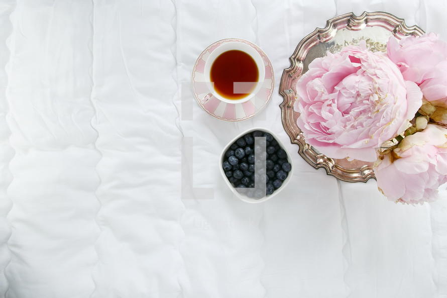 silver tray, cup of tea, bowl of blueberries, and peonies 