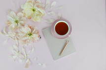 tea cup, flowers petals, journal, and pen on a pink background 