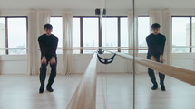 Talented male dancer choreographing contemporary dance, practicing graceful movements by mirror wall during rehearsal in studio. Full length shot
