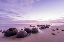 Round boulders on a beach at the edge of the ocean.