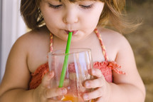 a toddler girl sipping a drink through a straw 