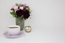 purple flower arrangement, candle, tea cup, on a table 