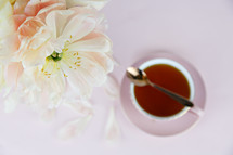tea cup, spoon, and petals on a pink background 