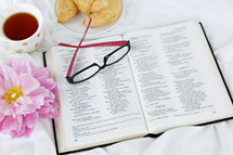 reading glasses, croissant, tea cup, open Bible, and pink flower 