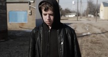 Young man, teenager outside on cold day with backpack and winter coat walking in cinematic slow motion. A young, teen boy walking to high school or young homeless man. 



