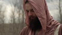 Jesus Christ dressed in brown robes and shroud walking alone in cinematic, slow motion in the wilderness temptation by the Devil or Satan for 40 days and 40 nights looks up to God in heaven in stoic, prayerful contemplation. Could also be used to depict a biblical prophet like Noah, Abraham, Elijah, Moses or John the baptist. 