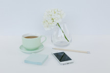 flowers in a vase, cup of tea, cellphone, notepad, and pencil 