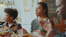 Little African American kids and their parents having meal, smiling and talking at home dinner with family
