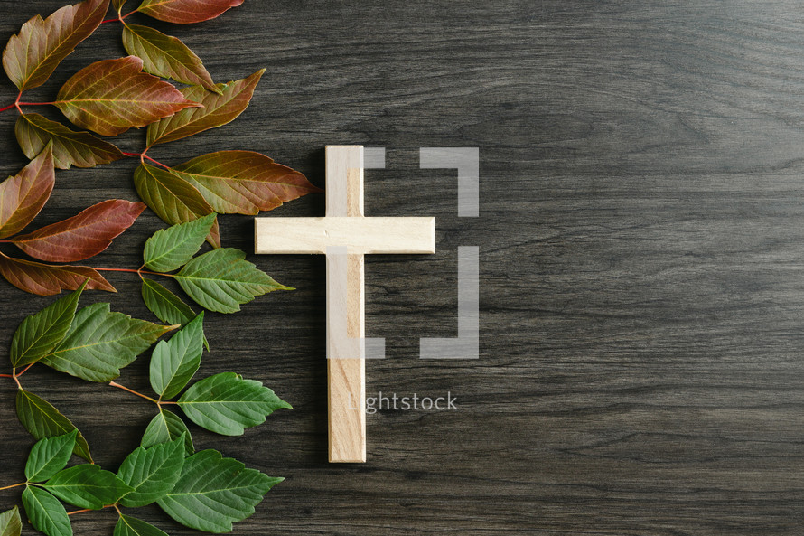 wooden cross and red and green leaves on a wood background 