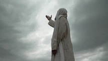 Religious Christian man, bible prophet or Jesus Christ with beard wearing a white tunic lifts hands to sky praying in worship to God.