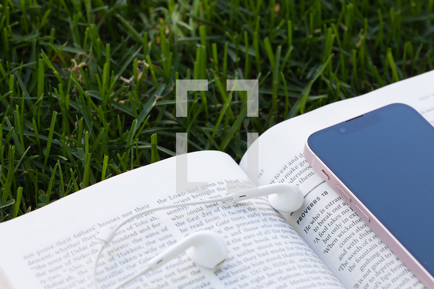  open bible, earbuds and cellphone in grass