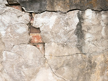 cracked exterior concrete wall surface revealing brick 