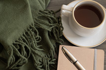 blanket, coffee cup, journal and pen 