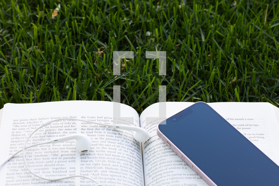 open bible, earbuds and cellphone in grass