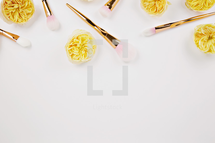 gold makeup brushes and gold flowers on pink 