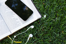 open bible, earbuds and cellphone in grass