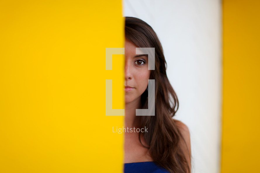 half of a woman's face peeking behind a yellow wall