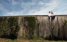 man and woman sitting on an ivy covered wall