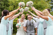 bride and groom walking under an arch of bouquets held high by bridesmaids 