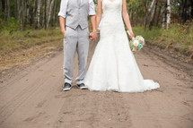 a bride and groom standing on a dirt road 