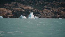 Icebergs In Argentino Lake Against The Mountain Seen From A Sailing Boat. - wide shot	